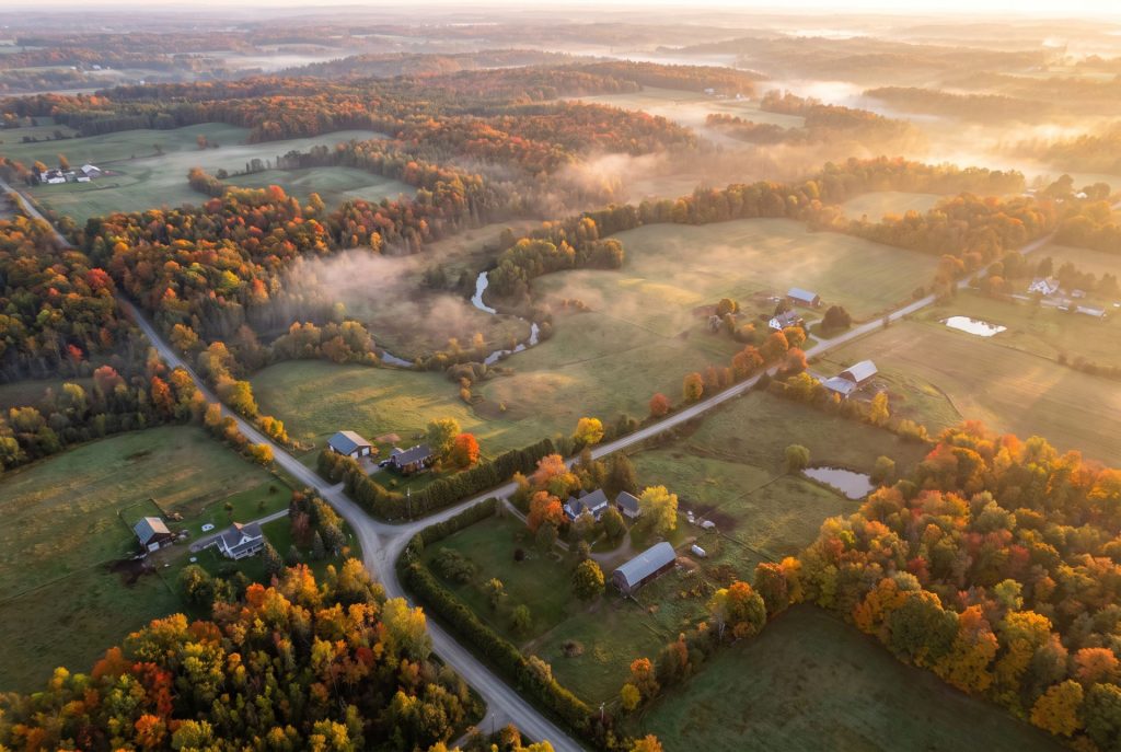 Beautiful Southern Ontario countryside during peak autumn colours with rolling farmland, mature maple trees and a scenic country road.